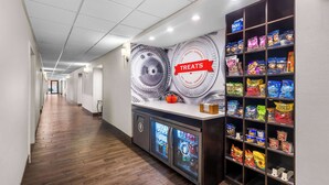 A hallway with a snack bar featuring a variety of packaged snacks and a refrigerated display. - Hampton Inn Marion (Marion)