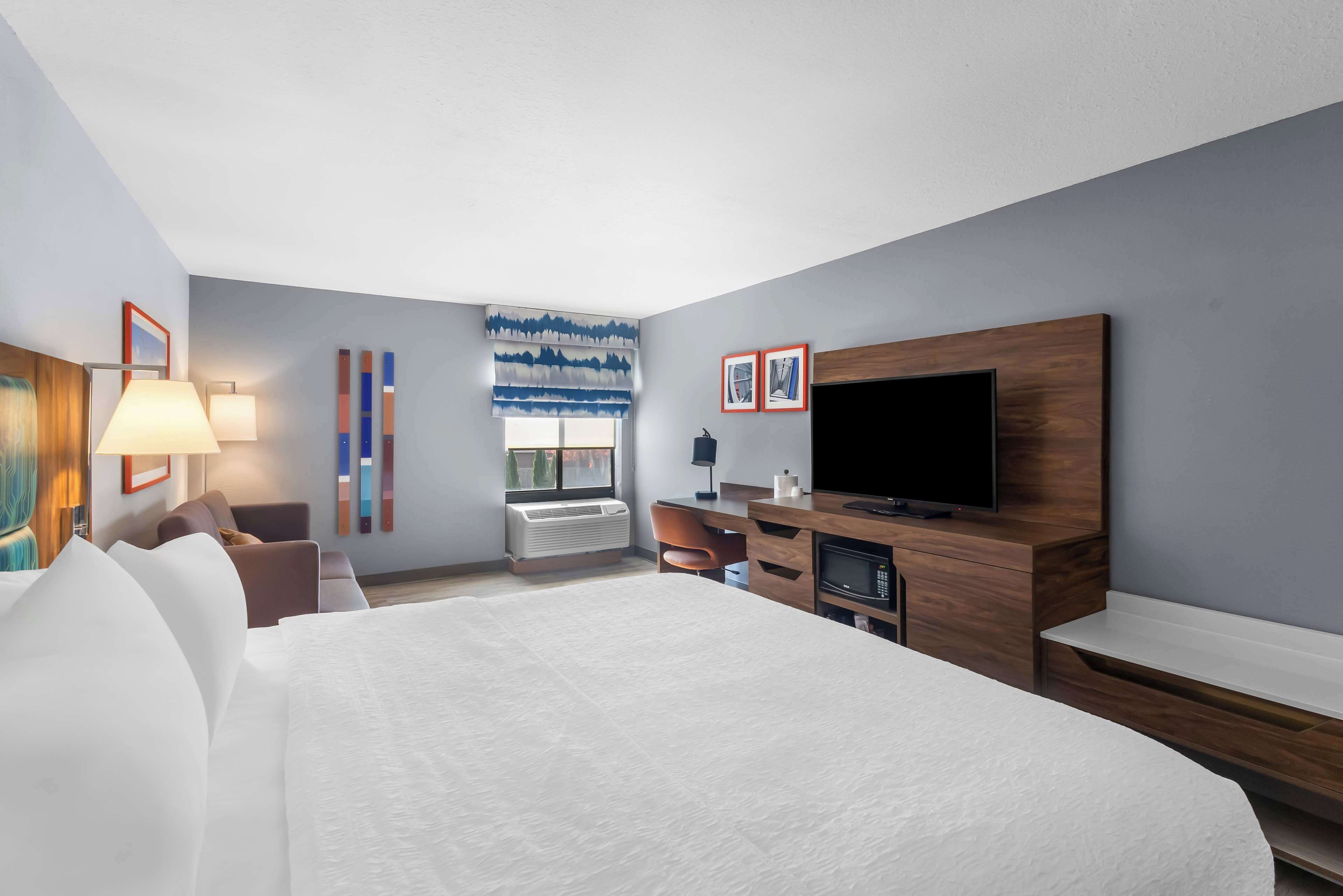 Habitación de hotel moderna con una cama grande, un televisor de pantalla plana, un escritorio y una ventana con vistas a árboles.