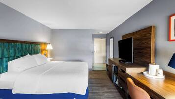 Habitación de hotel con cama, escritorio, televisor y puerta que da a otra habitación.