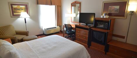 Habitación de hotel con cama, escritorio, silla, televisor, microondas y lámpara.