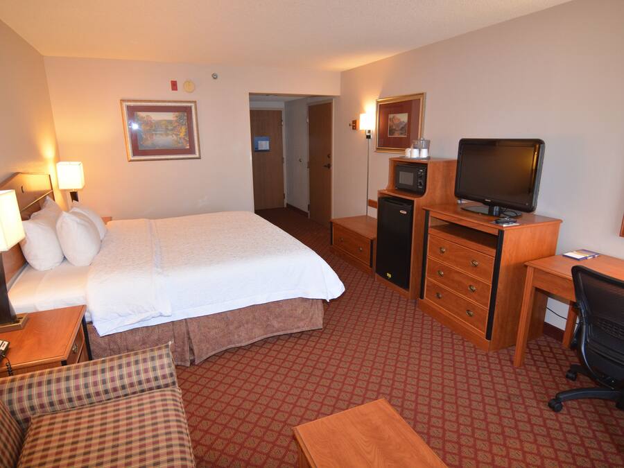 Una habitación de hotel con cama, escritorio con computadora, televisor, silla y una mesita.