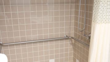 A shower area with a tiled floor, a grab bar, and a showerhead.