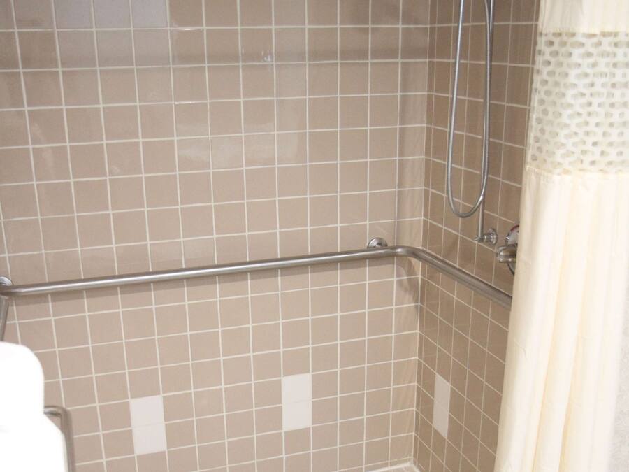 A shower area with a tiled floor, a grab bar, and a showerhead.