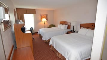 A hotel room with two beds, a desk, a chair, and a desk lamp.