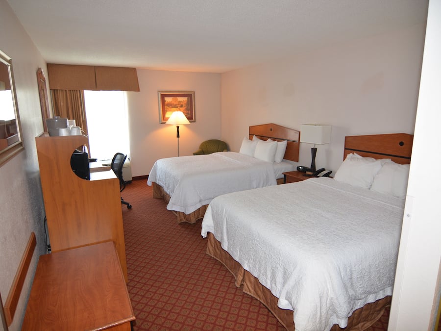 A hotel room with two beds, a desk, a chair, and a desk lamp.