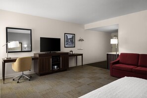 A hotel room with a bed, a desk with a TV, a chair, a red sofa, and a mirror. - Hampton Inn Morristown (Morristown)