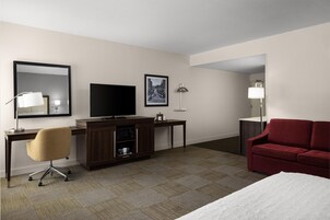 Habitación de hotel con cama, escritorio con televisor, una silla, sofá rojo y espejo.