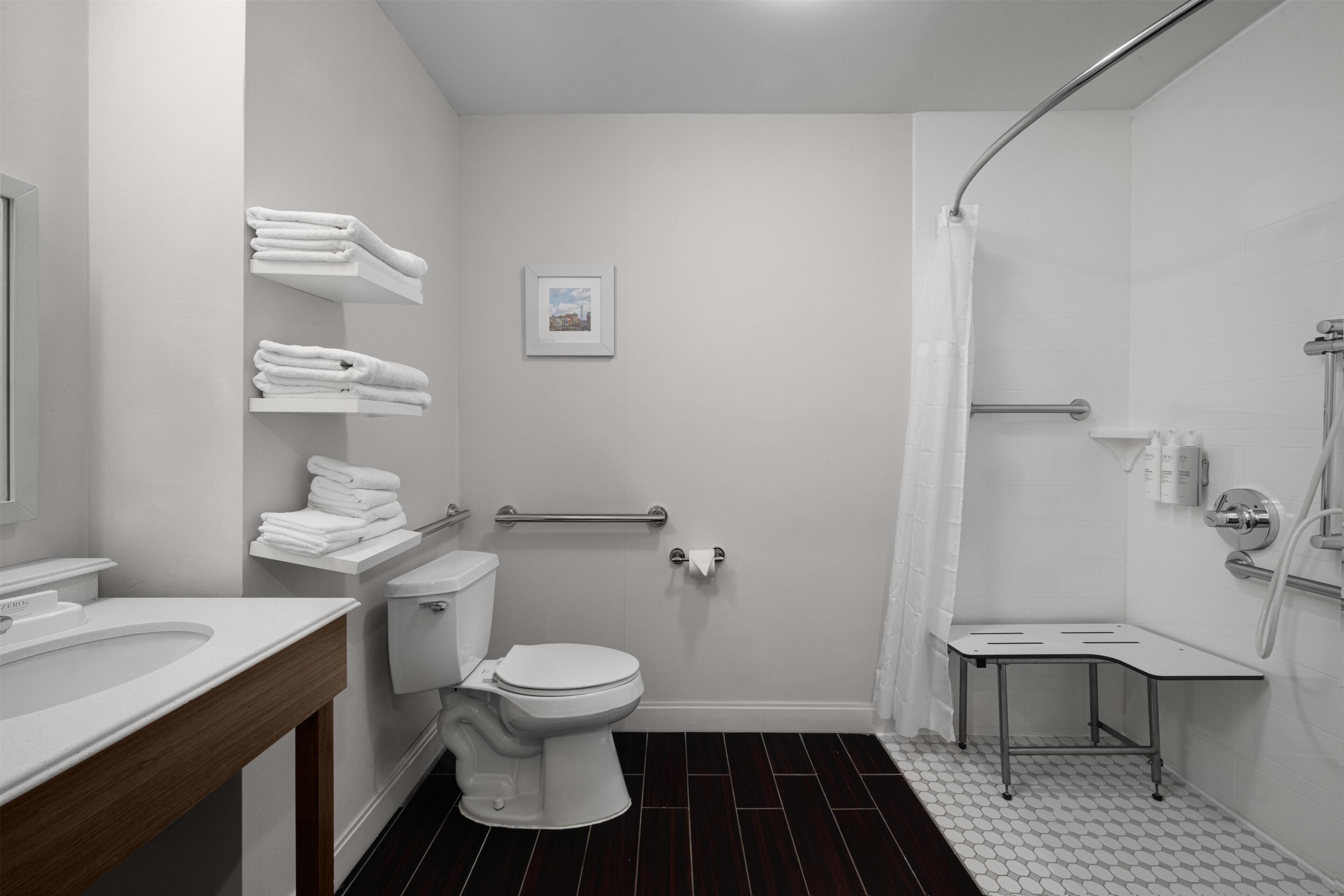 A bathroom with a toilet, sink, towel racks, shower, and a small table.