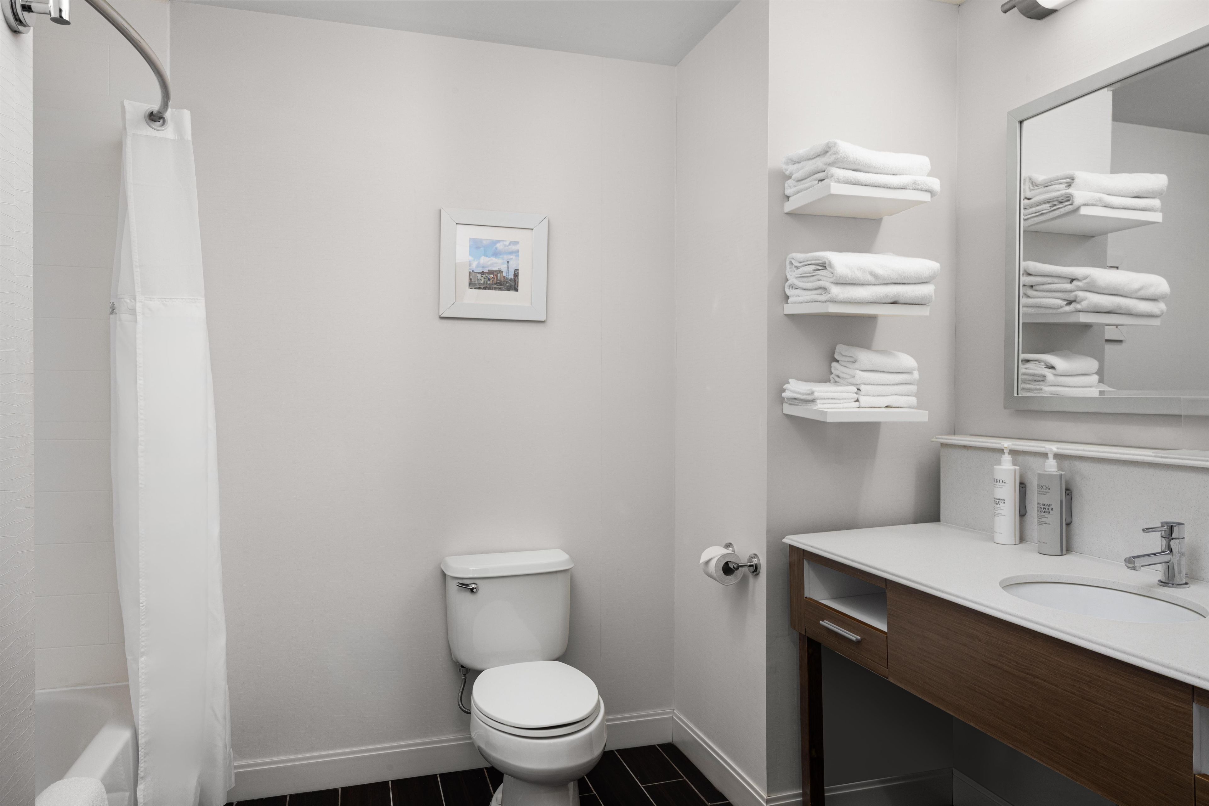 Un baño moderno con inodoro, ducha, lavamanos y un perchero para toallas.