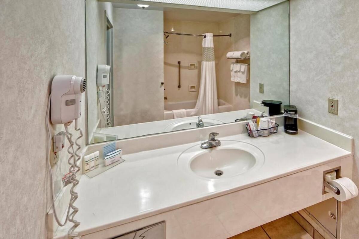 A bathroom with a large mirror, a sink, a hairdryer, and a shower area.