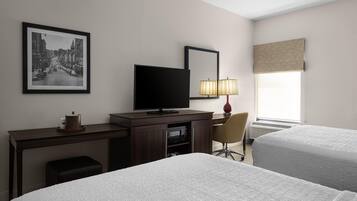 A hotel room with two beds, a desk with a television, a chair, a lamp, and a framed picture on the wall.