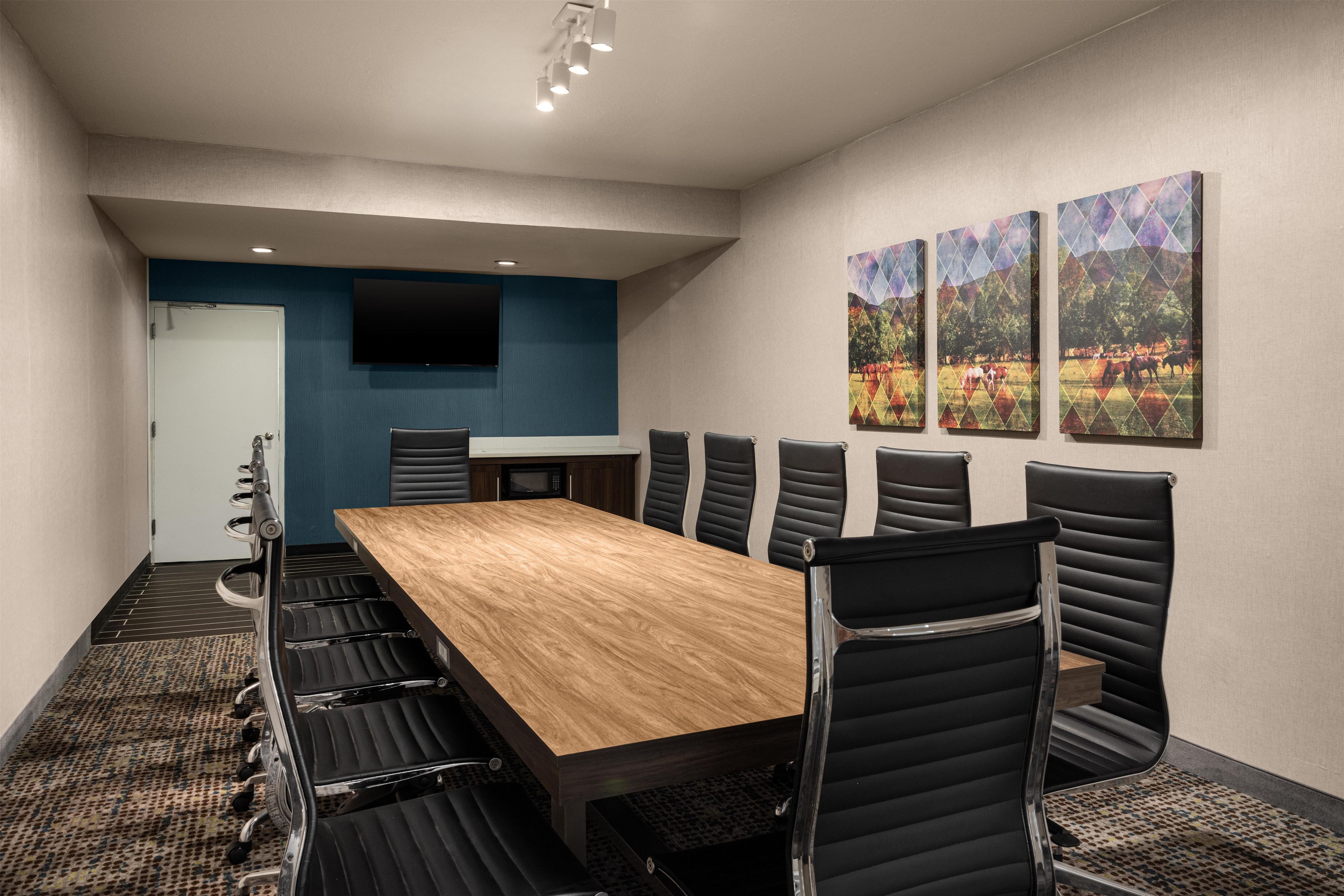 A conference room with a long table, black chairs, a flat-screen TV, and three framed pictures on the wall.