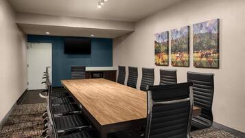 A conference room with a long table, black chairs, a flat-screen TV, and three framed pictures on the wall.