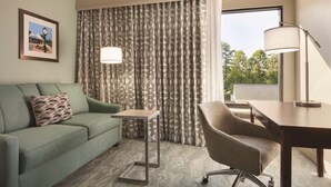 Een hotelkamer met een groene bank, een klein bijzettafeltje, een bureau met stoel, behang met patroon en een ingelijst kunstwerk aan de muur.