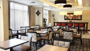 Een restaurant in een hotel, met meerdere tafels en stoelen, een bar en een groot raam met gordijnen.