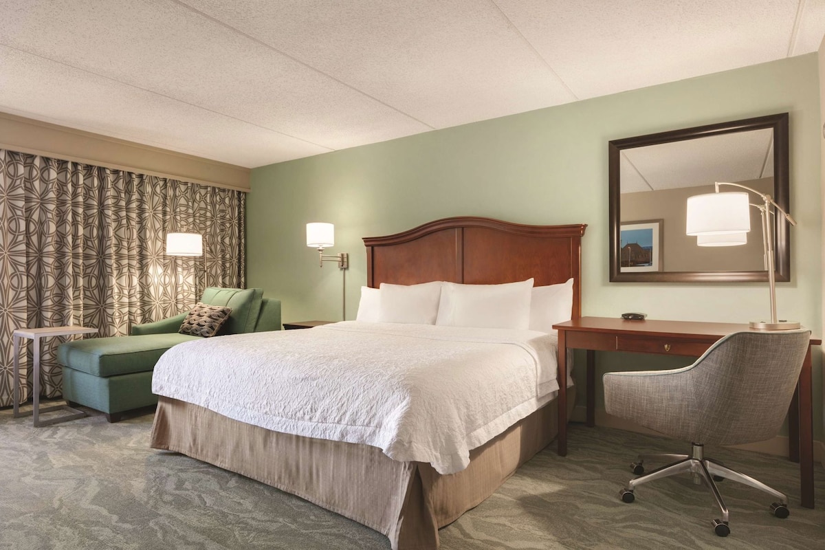 Een hotelkamer met een bed, een bureau, een stoel, een lamp en een kamerkleed met een patroon.