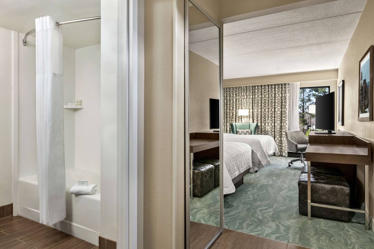 Une chambre d’hôtel équipée d’une douche, d’un lit avec un bureau, d’une chaise, d’une petite table et d’un miroir.