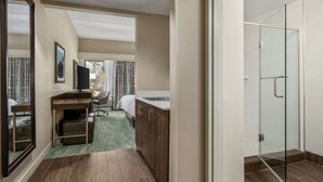 Een hotelkamer met een bureau, stoel, bed en een douche met glazen wanden.