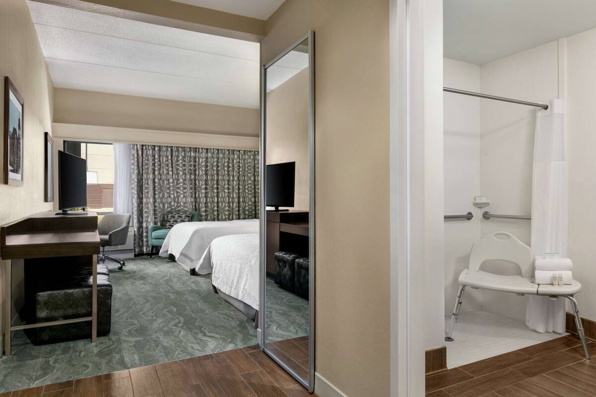 Une chambre d’hôtel comprenant un lit, un bureau, une chaise, un siège de douche et un miroir.