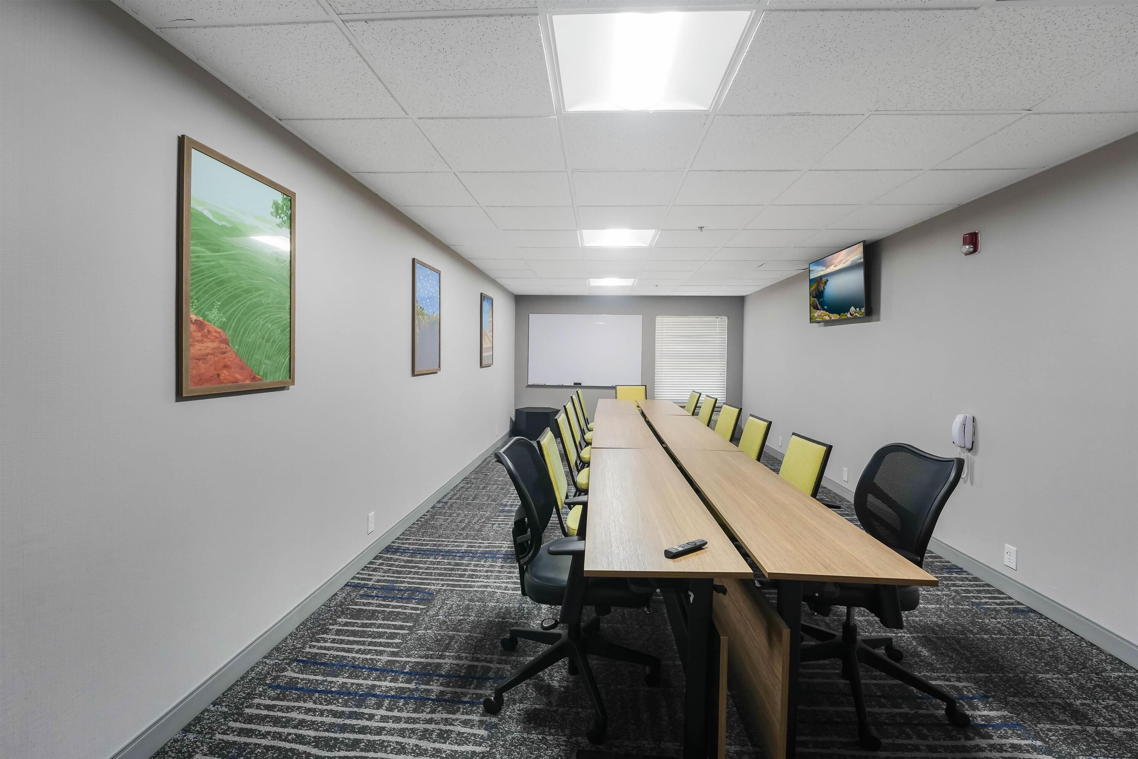 Uma sala de conferências com uma mesa comprida, cadeiras, uma tela de projetor e quadros nas paredes.