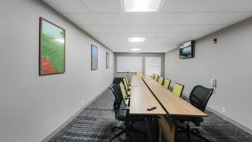 Uma sala de conferências com uma mesa comprida, cadeiras, uma tela de projetor e quadros nas paredes.