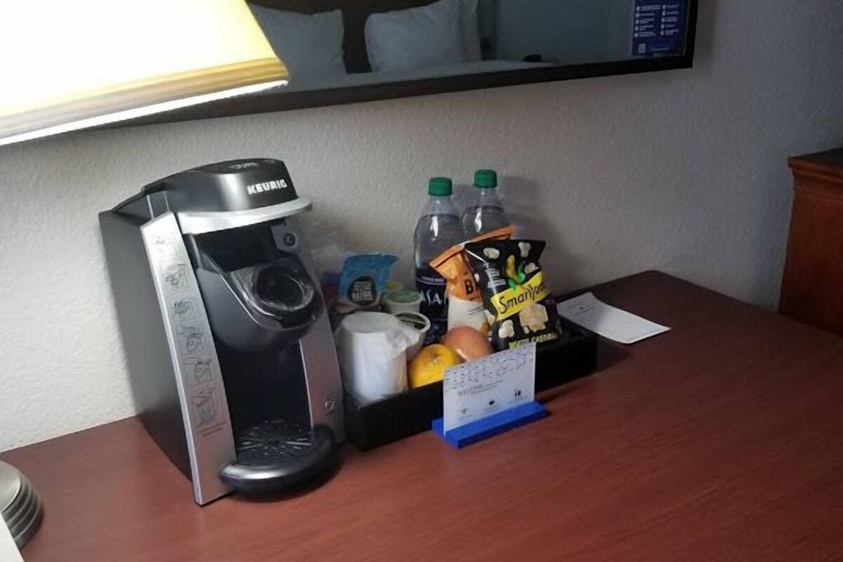 Quarto de hotel com cafeteira, garrafas de água, lanches e balcão de recepção.