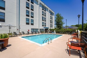 A swimming pool with lounge chairs and a building with multiple windows in the background. - Hampton Inn Henderson (Henderson)