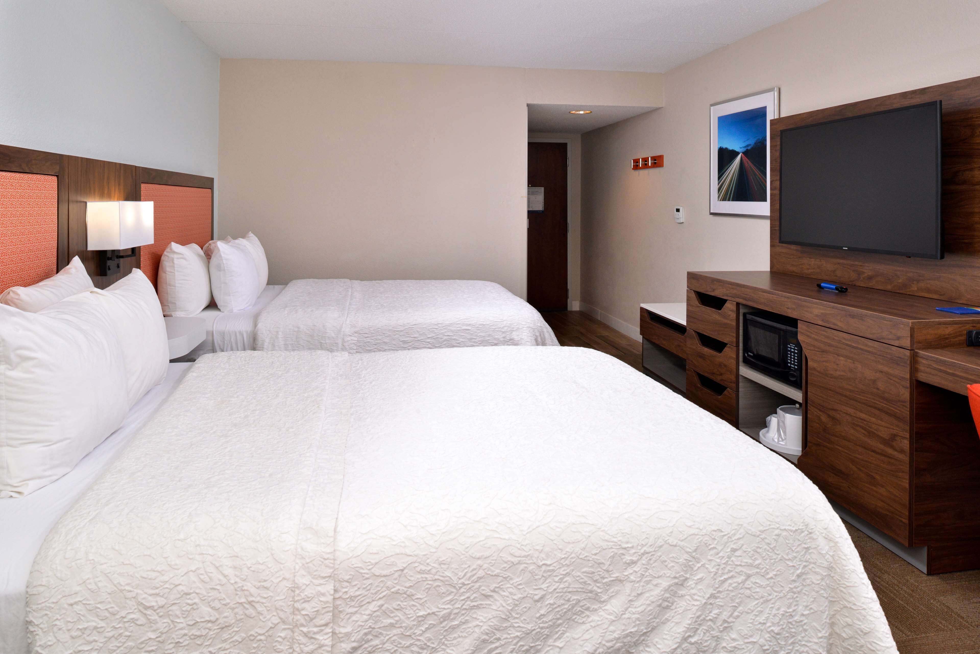 Habitación de hotel con dos camas, televisión, microondas y un escritorio pequeño.