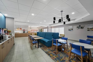 Una cafetería moderna con un sofá azul, mesas y sillas de madera, una zona de cocina y un tapete colorido.