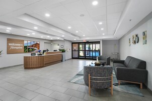 A hotel reception area with a reception desk, a seating area with a sofa and chairs, and a wall-mounted sign.