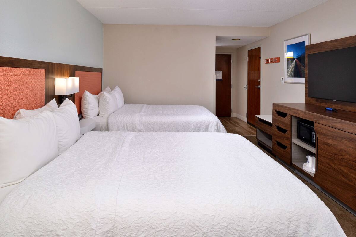 Quarto de hotel com duas camas, uma televisão e uma cômoda de madeira.