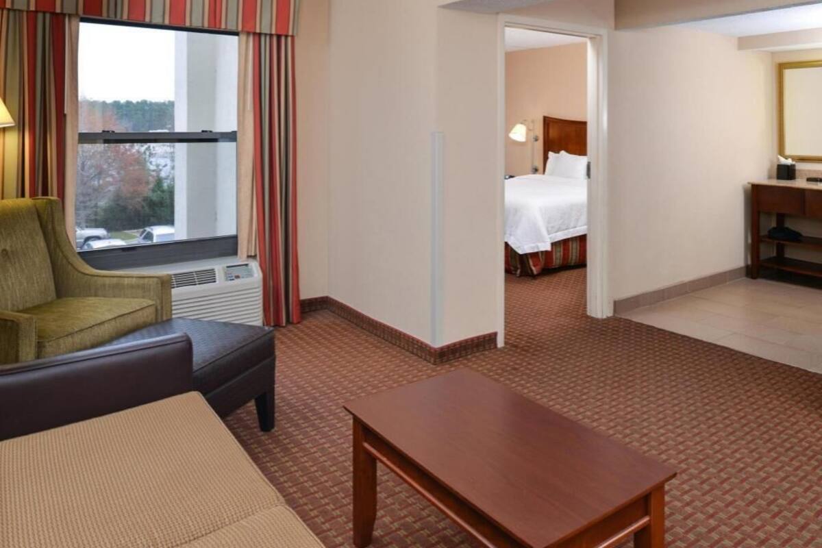 Quarto de hotel com cama, escrivaninha, cadeira, janela com cortinas e vista para o exterior.