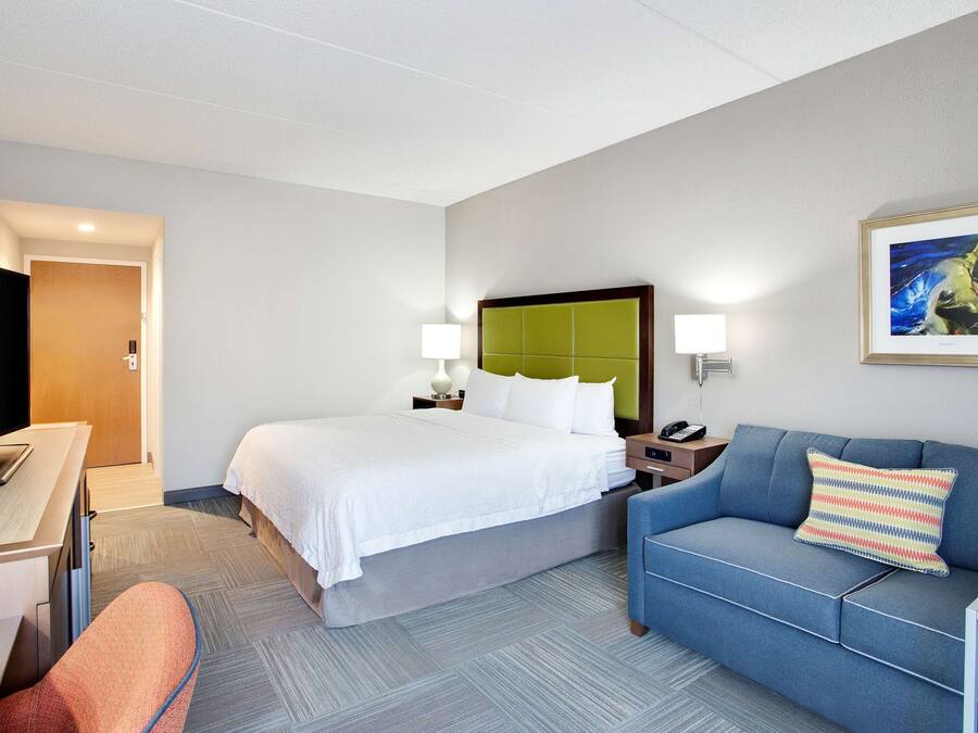 A hotel room with a bed, a desk, a blue sofa, a TV, and a framed picture on the wall.