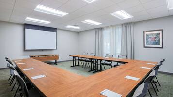 A conference room with a long wooden table, multiple chairs, a projector screen, and a framed picture on the wall.