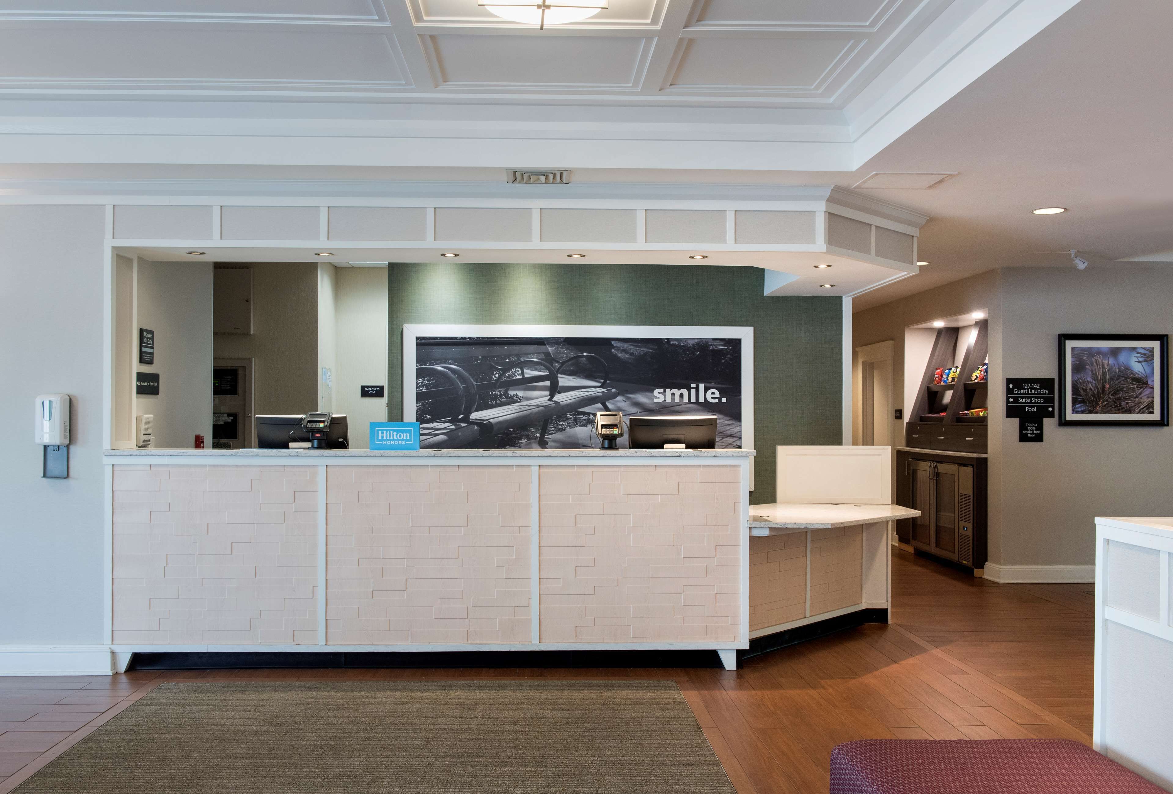 A reception area with a white reception desk, a large framed poster, and a small blue sign.
