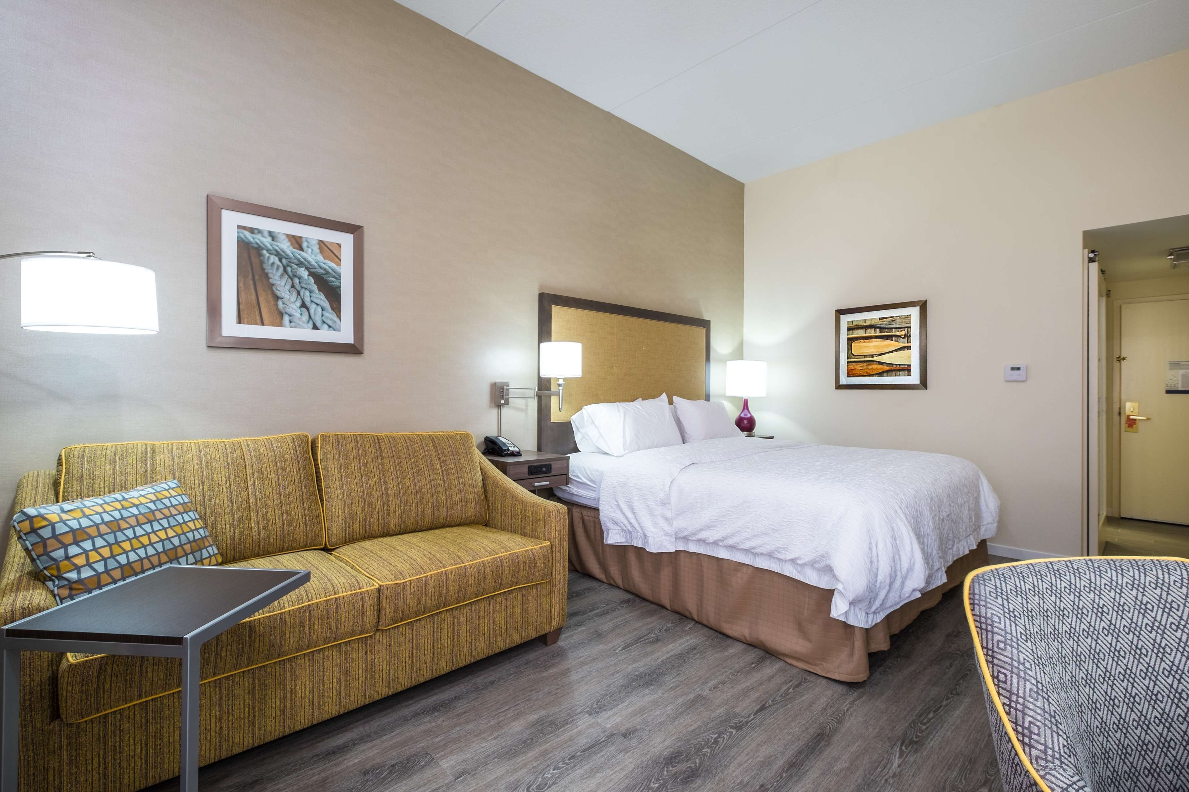 A hotel room with a sofa, a bed, a nightstand, a lamp, and a chair.