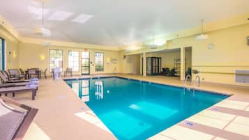 A swimming pool with lounge chairs and sunbeds, a ceiling with skylights, and a clock on the wall.