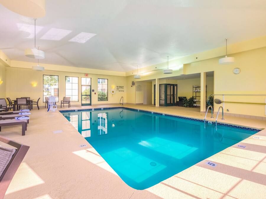 A swimming pool with lounge chairs and sunbeds, a ceiling with skylights, and a clock on the wall.
