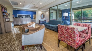 A spacious lobby with a blue wall, a reception desk, a large mirror, and seating areas with a patterned table and chairs.