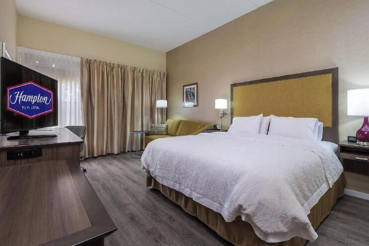 A hotel room with a bed, a desk, a television, and a nightstand with a lamp.