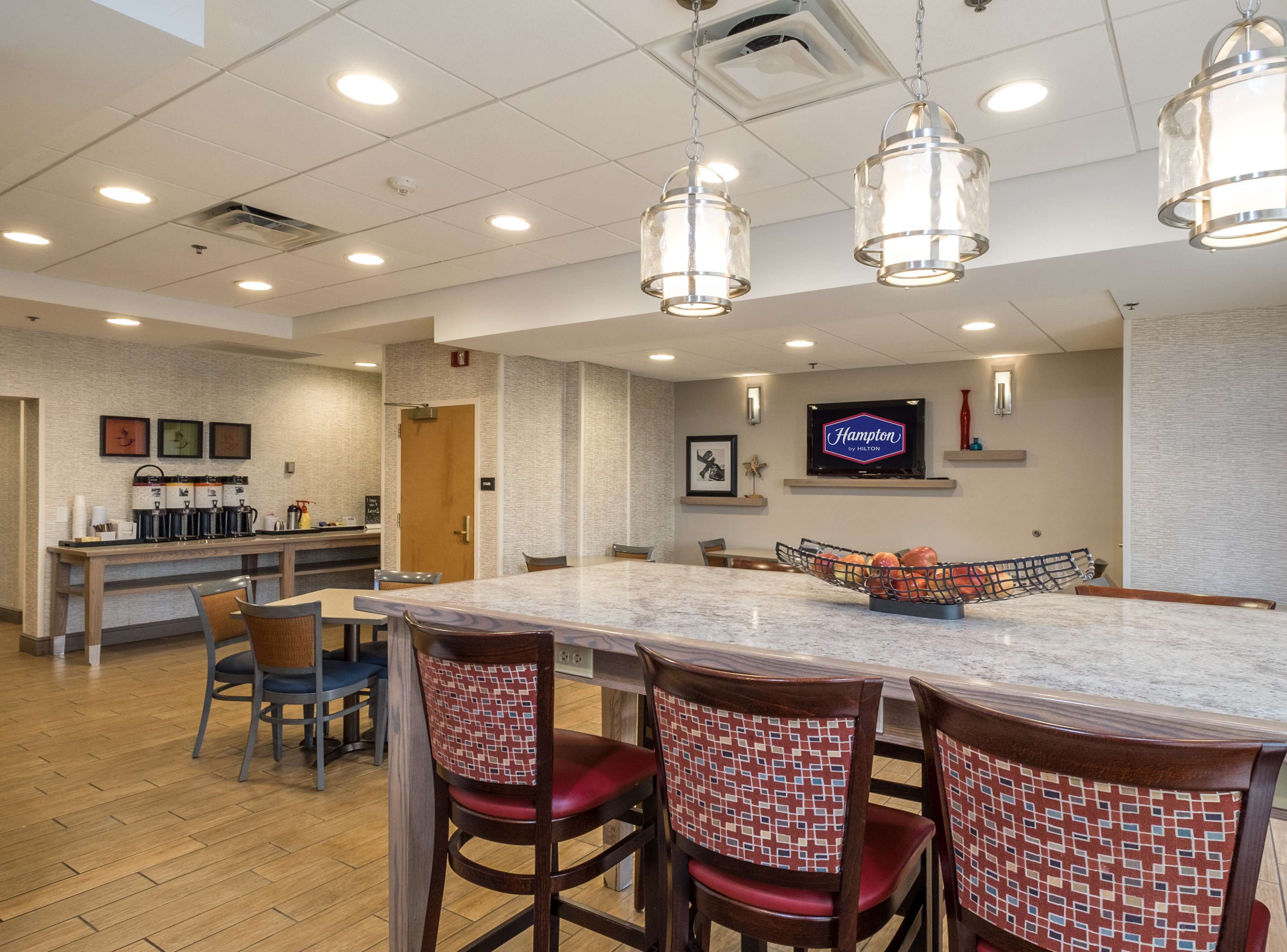 A hotel lobby with a marble reception desk, seating area, and a television displaying 'Hampton by Hilton'.
