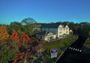 A Hampton Inn by Hilton hotel with a large building, a parking area, and surrounding trees.