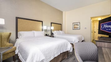 Una habitación de hotel con dos camas, una silla, un escritorio, un televisor y un cuadro en la pared.