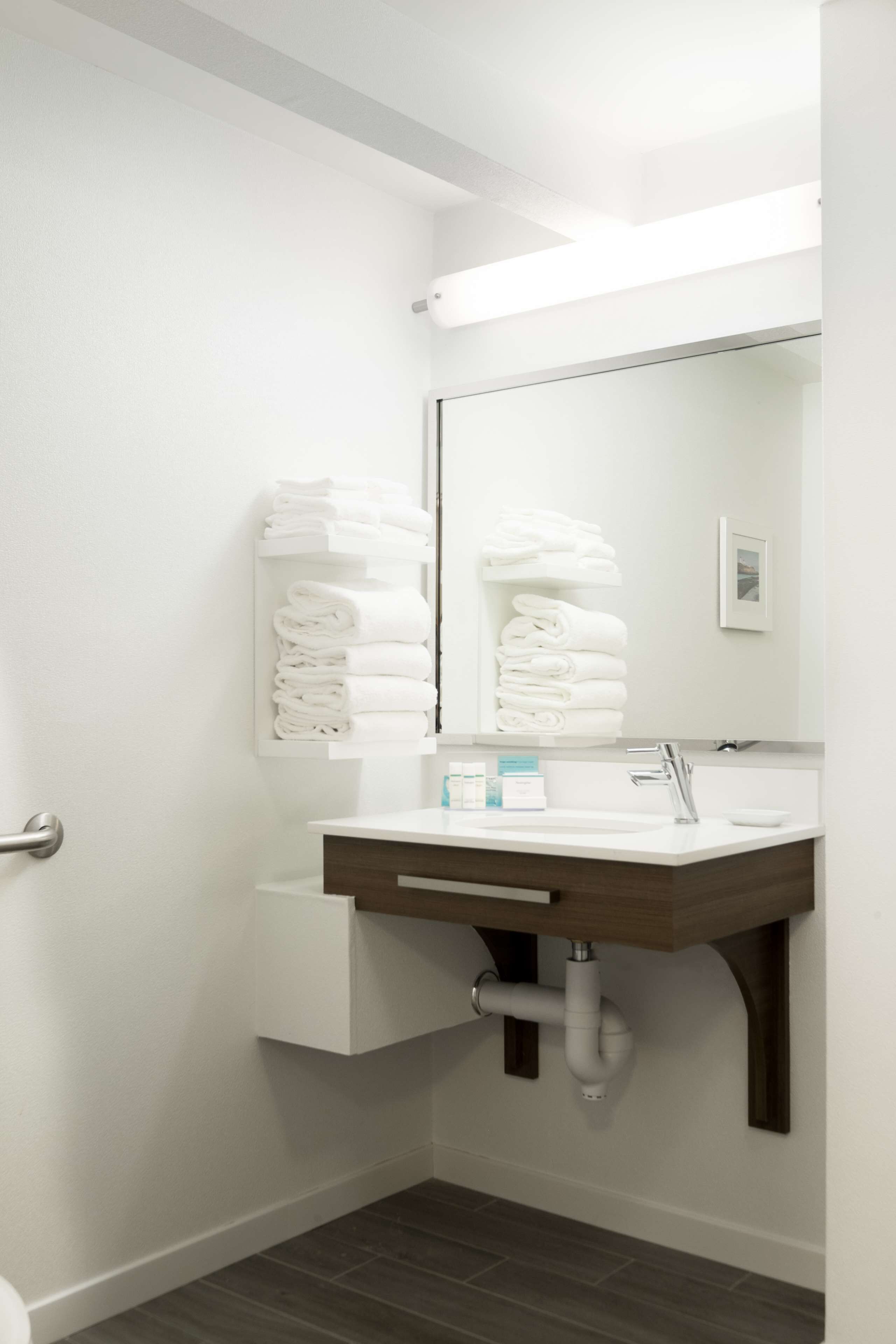 Une salle de bain moderne avec un lavabo blanc, un miroir et des serviettes soigneusement pliées et rangées sur une étagère.