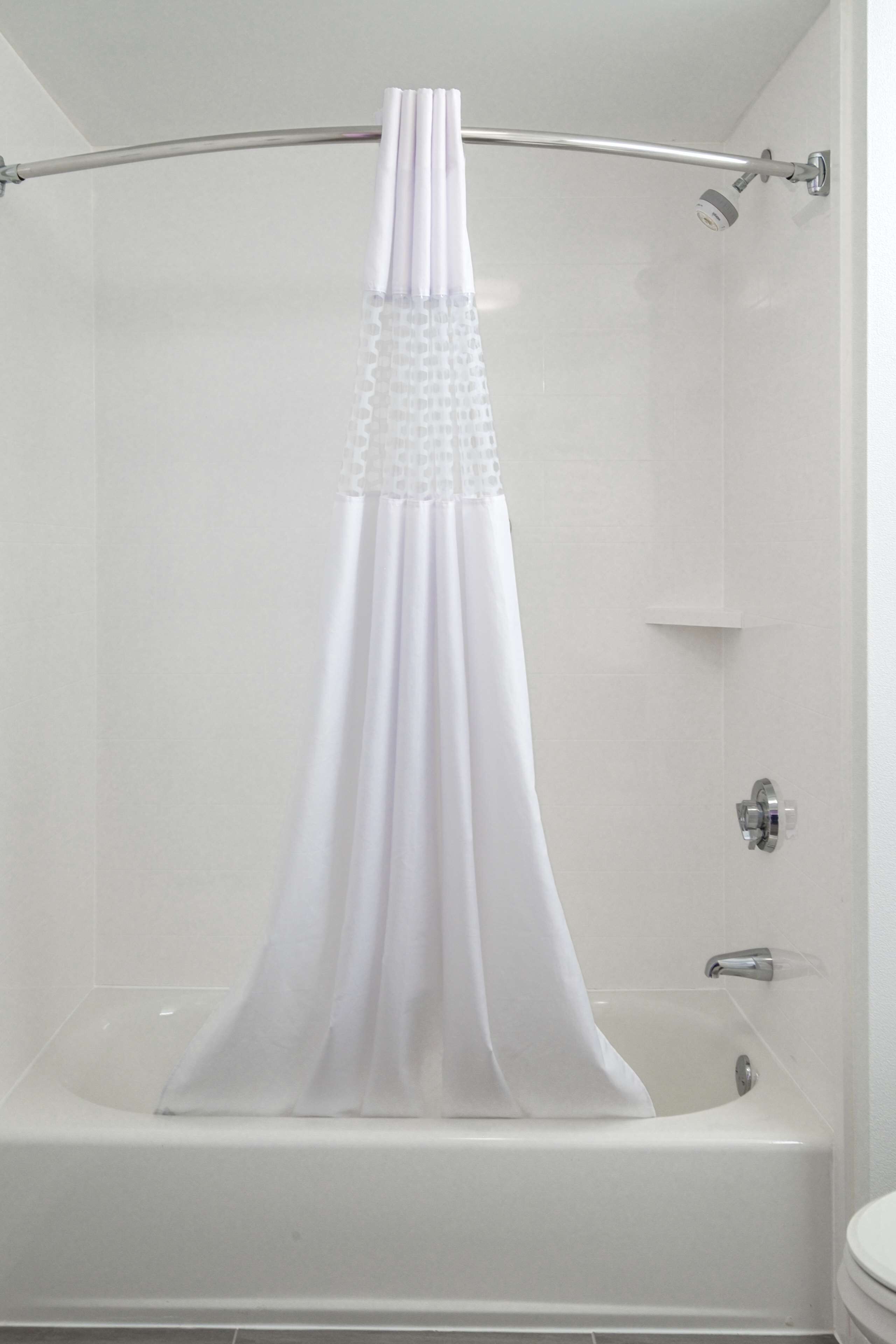 Une baignoire blanche avec un rideau de douche, une douchette et un robinet fixé au mur.
