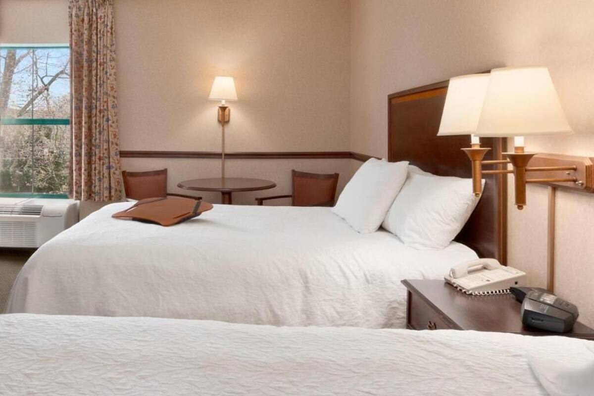 A hotel room with a bed, bedside table, lamp, and a window with curtains.