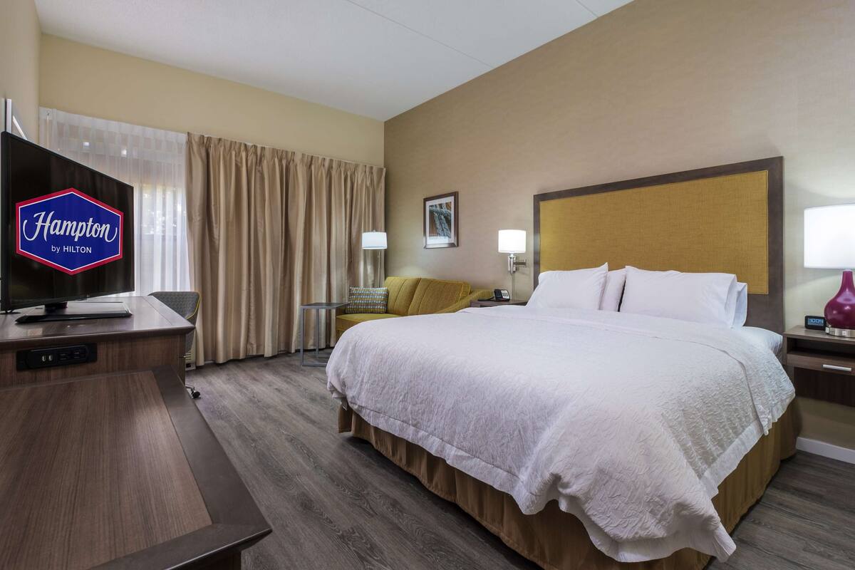 A hotel room with a bed, a TV, a desk, and a lamp.
