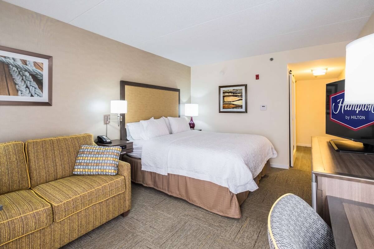A hotel room with a bed, a sofa, a desk, and a television.