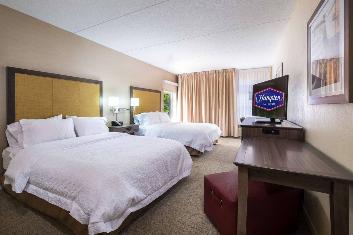 A hotel room with two beds, a desk, a television, and a framed picture on the wall.