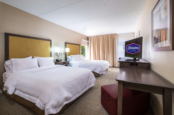 A hotel room with two beds, a desk, a television, and a framed picture on the wall.